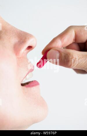 Femme de mettre une pilule rouge dans sa bouche. Banque D'Images