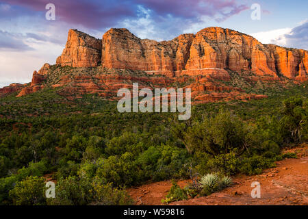 Beautiful red rock formation éclairé par le coucher du soleil au-dessus d'un paysage contrasté de Juniper et arbustes verts sous un ciel coloré - Sedona, Arizona Banque D'Images