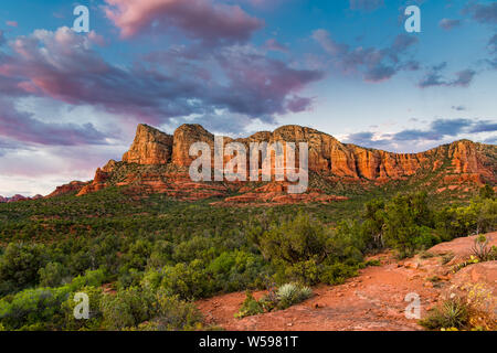 Coucher du soleil illumine un magnifique paysage de formations de roche rouge et vert forêt de genévrier en dessous d'un ciel bleu avec des nuages roses et mauves Banque D'Images