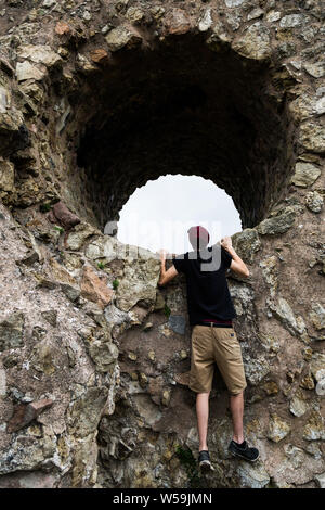 Un jeune'regarde à travers l'oeil de la sorcière à l'Engelbourg médiévale ruinée château à proximité de la ville alsacienne de Thann, France. Banque D'Images