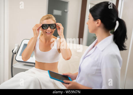 Faire vous-même sans danger. Femme assise devant son cosmetologist mise sur les procédures avant de lunettes de protection. Banque D'Images