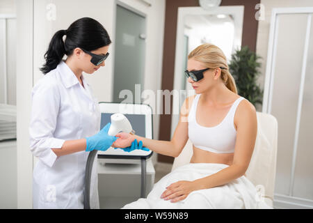 Soins Professionnels. Jeune femme assise concentré devant elle sa main donnant cosmetologist d'avoir ses procédures spa dans un salon de beauté. Banque D'Images