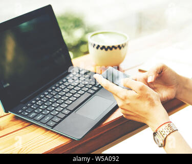 Close-up of female hands holding a mobile phone sms, dans le contexte d'un ordinateur portable et d'une tasse de thé sur la table par la fenêtre dans un café Banque D'Images