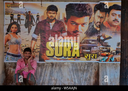 Un homme s'accroupit en face d'une affiche pour un film Hindi (qualifiée de son orig. Tamil), dans un petit cinéma de la classe ouvrière dans la région Khetwadi, Mumbai, Inde Banque D'Images