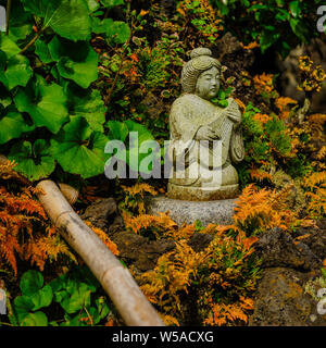 Petite statue avec de riches illustrations détaillées placés sur des roches entourée de fleurs à Kamakuras Hase-dera, Japon Novembre 2018 Banque D'Images