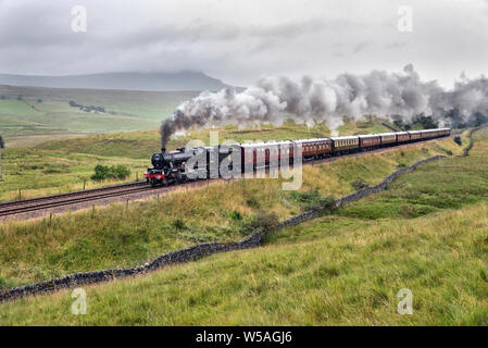 Ribbesdale, North Yorkshire, UK. 27 juillet, 2019. L'ascension de la pente raide sur la célèbre ligne de chemin de fer Settle-Carlisle par temps humide dans le Yorkshire Dales, locomotive à vapeur 'Leander' avec 'le' Hadrien spécial, c'est vu à Armoy, près de Horton-en- Ribblesdale. Pen-y-ghent pic est vu sous nuage à l'horizon. Crédit : John Bentley/Alamy Live News Banque D'Images