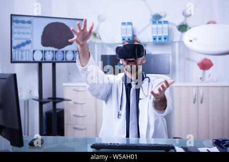 Avis d'un médecin homme tenant un rendu 3D à l'aide de casque de réalité virtuelle. Médecin dans son bureau à travailler. Banque D'Images