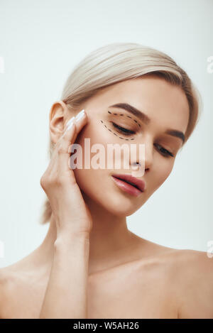 Avant l'opération opération. Portrait de belle jeune femme blonde en gardant les yeux fermés et de toucher son visage avec des lignes noires sur les paupières et chirurgicale sous les yeux. Concept de beauté. Lifting. La chirurgie en plastique Banque D'Images