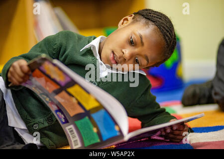 Une jeune fille afro-antillaise la lecture dans une bibliothèque de l'école primaire au Royaume-Uni Banque D'Images