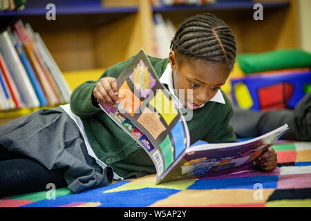 Une jeune fille afro-antillaise la lecture dans une bibliothèque de l'école primaire au Royaume-Uni Banque D'Images