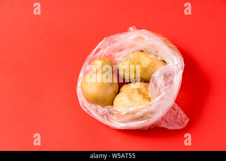 Vue avant les pommes de terre dans un sac plastique sur fond rouge. Image montre le harmness à l'aide de sacs de stockage de l'alimentation artificielle. Banque D'Images