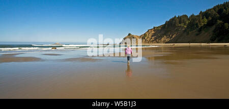 Une femme prend une plage à pied sur une grande plage de sable sur la côte du Pacifique de l'Oregon, près de la ville de Lincoln City, Oregon. Banque D'Images