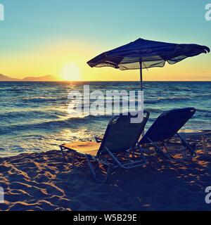 Chaises longues et parasol sur la plage au coucher du soleil par la mer. Beau concept pour les vacances, vacances d'été et les voyages. Banque D'Images