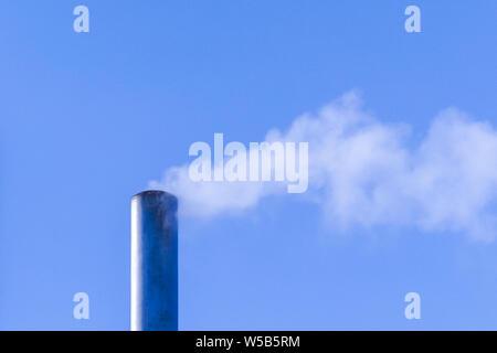 Le tuyau de presse de la fumée dans le ciel bleu et pollue l'environnement. Problème écologique. Banque D'Images