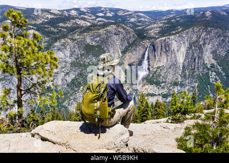 Randonneur non identifié, assis sur un rocher et regardant vers la Vallée Yosemite Yosemite Falls et supérieure, Yosemite National Park, Californie Banque D'Images