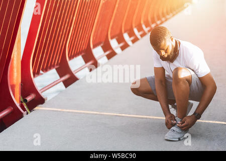 Les jeunes afro man checking sur ses lacets dans la lumière du soleil Banque D'Images
