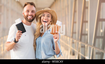 Heureux couple smiling avec les billets et les passeports à l'aéroport Banque D'Images