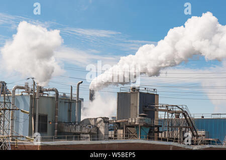 Pollution atmosphérique s'élève de cheminée d'usine contre un ciel bleu Banque D'Images