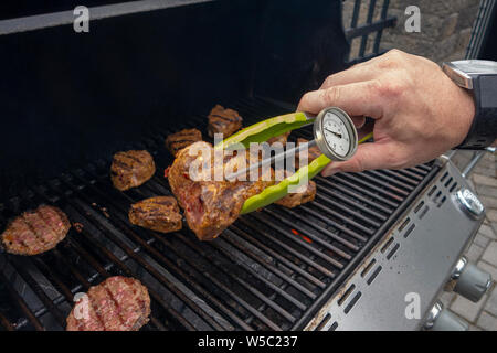 Les hamburgers et les côtelettes d'agneau sur un barbecue en plein air avec barbecue et cuire la température viandes cheacking langues Banque D'Images