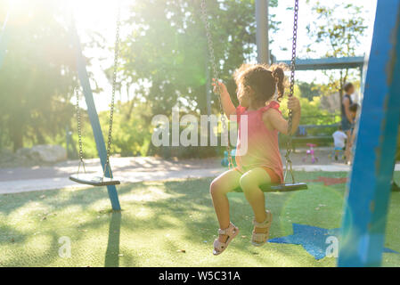 Happy child girl laughing et se balancer sur une balançoire à l'aire en été. Banque D'Images