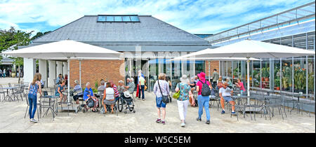 RHS Wisley les gens marchent à nouveau l'entrée du bâtiment café moderne avec parasol ombre & tables Jardins de la Royal Horticultural Society Surrey England UK Banque D'Images