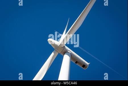 Une éolienne contre un ciel bleu, avec un avion passant par en arrière-plan Banque D'Images