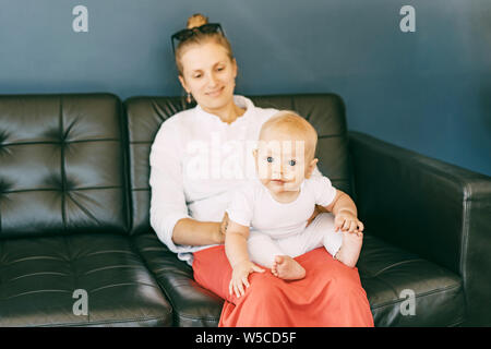 bébé regarde curieusement l'appareil photo tout en étant assis aux genoux de sa mère Banque D'Images