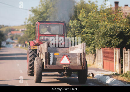 Vieux tracteur dans les rues d'un village rural en Roumanie avec beaucoup de végétation autour de Banque D'Images