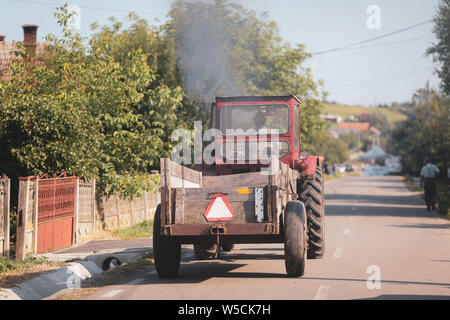 Vieux tracteur dans les rues d'un village rural en Roumanie avec beaucoup de végétation autour de Banque D'Images