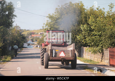 Vieux tracteur dans les rues d'un village rural en Roumanie avec beaucoup de végétation autour de Banque D'Images