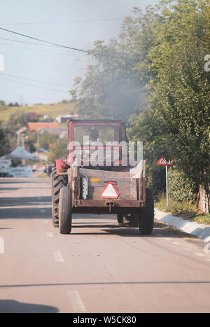 Vieux tracteur dans les rues d'un village rural en Roumanie avec beaucoup de végétation autour de Banque D'Images