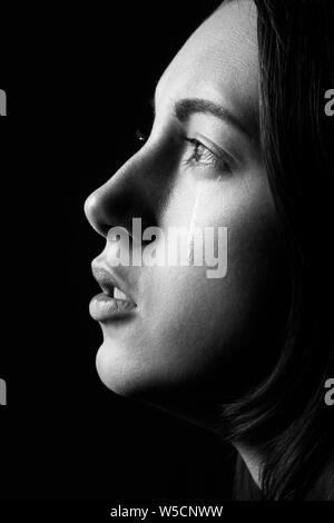 Femme triste à pleurer, à côté sur fond noir, closeup portrait, vue de profil, monochrome Banque D'Images