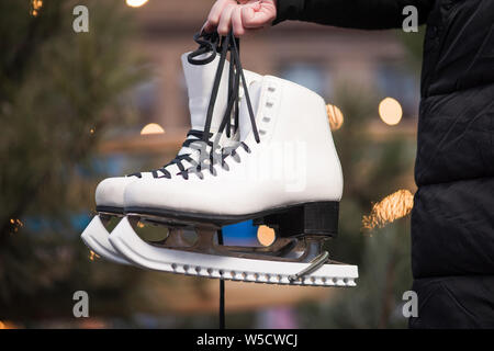 Jeune femme tenant une paire de patins blancs sur fond de lumières du soir. Banque D'Images