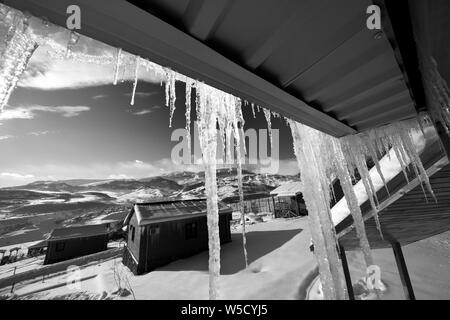 Pavillon avec grand soleil, les glaçons et les petites maisons en bois à l'hiver enneigé des montagnes. Montagnes du Caucase, l'Azerbaïdjan, Shahdagh. Vue grand angle. Black et w Banque D'Images