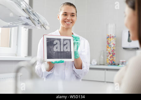 Portrait of smiling female dentist showing dents x-ray image pour le patient pendant la consultation en clinique, copy space Banque D'Images