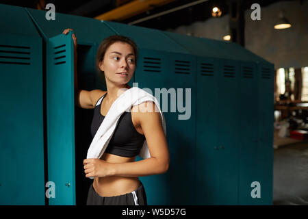 Jusqu'à la taille spectaculaire portrait of young woman standing by casier dans sports club et à l'écart, copy space Banque D'Images