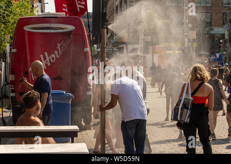 Montréal, CA - 27 juillet 2019 : Les gens de marcher sous système de brumisation pour se rafraîchir (MIST) système de refroidissement lors de canicule dans le quartier des festivals. Banque D'Images