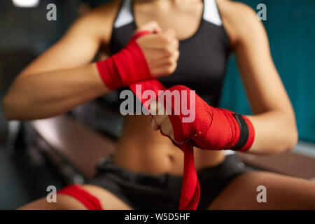 Close up of tough young woman putting on main rouge s'enroule la préparation à la pratique de la boxe en club de sport, copy space Banque D'Images