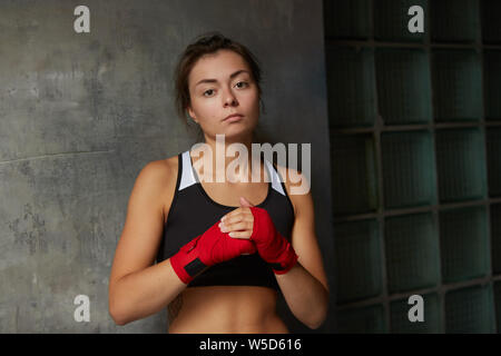 Taille portrait de femme difficile fighter wearing red hand wraps à la caméra à tout en se posant contre mur en béton, copy space Banque D'Images