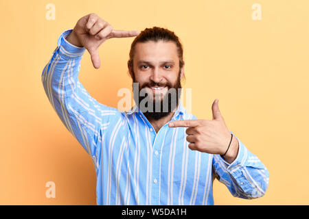Positive heureux beau jeune homme qui cadre avec les doigts isolé sur fond jaune. appareil photo. l'homme est prétendant qu'il est en train de prendre une photo Banque D'Images