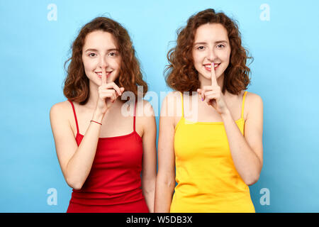 Chut signe. Deux belles femmes à la caméra en signe de silence. Studio shot, sur fond bleu.jumeaux partageant secrets. Le langage du corps Banque D'Images