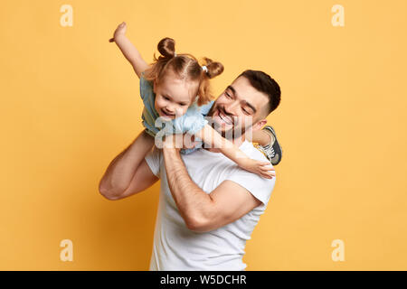 Cheerful homme heureux doux enseignement belle fille de voler comme un avion. la photo en gros. fond jaune isolé. studio shot, moments heureux avec bes Banque D'Images