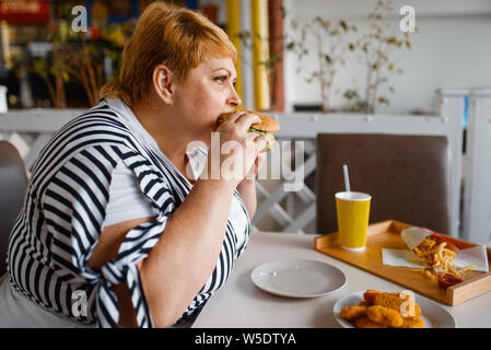 Fat Woman eating burger dans mall food court Banque D'Images