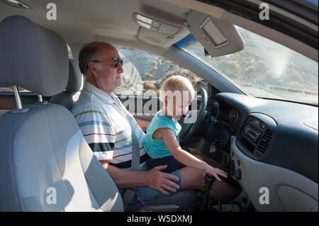 Boy driving car sur les grands-pères lap Banque D'Images