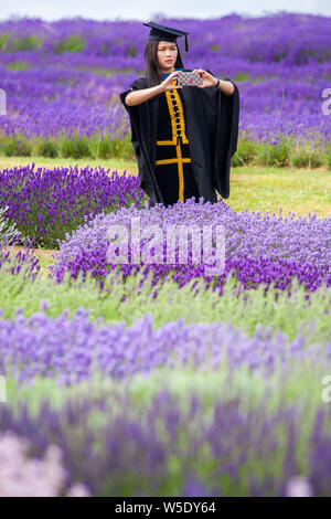 Jeune femme diplômée en cap and gown qui pose pour des photos dans les champs de lavande à Cotswold Lavender près de Broadway Worcestershire, Angleterre, Royaume-Uni Banque D'Images