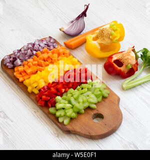 Les légumes frais, haché (carotte, céleri, oignon, poivrons de couleur) disposés sur une planche à découper en bois blanc sur un arrière-plan, Vue de côté. Banque D'Images