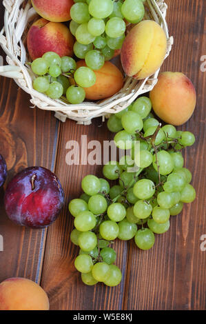 Raisins verts crus, d'abricots et de prunes sur la table en bois et un panier de fruits, vue supérieure selective focus Banque D'Images