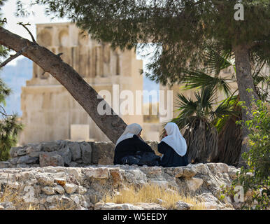 Deux femme musulmane s'asseoir et parler sur une paroi de rochers à l'ombre d'un arbre sur la citadelle d'Amman, en Jordanie. Banque D'Images