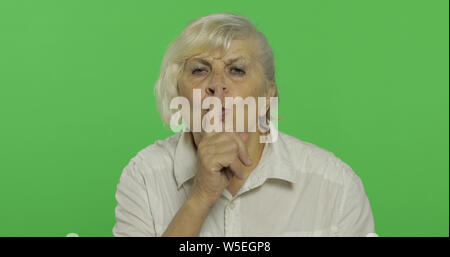 Une femme âgée montrant shh geste. Garder un secret ou pour demander le silence. Jolie vieille grand-mère dans une chemise blanche. Place pour votre logo ou texte. Le Chroma key. Arrière-plan de l'écran vert Banque D'Images