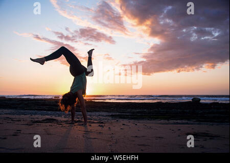 Coucher du soleil sur la plage de yoga avec yogi happy woman doing a handstand entrain sauvage. Banque D'Images